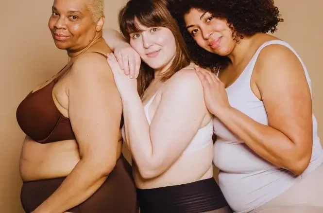 Three overweight women holding each other and smiling, supporting one another on a weight loss journey